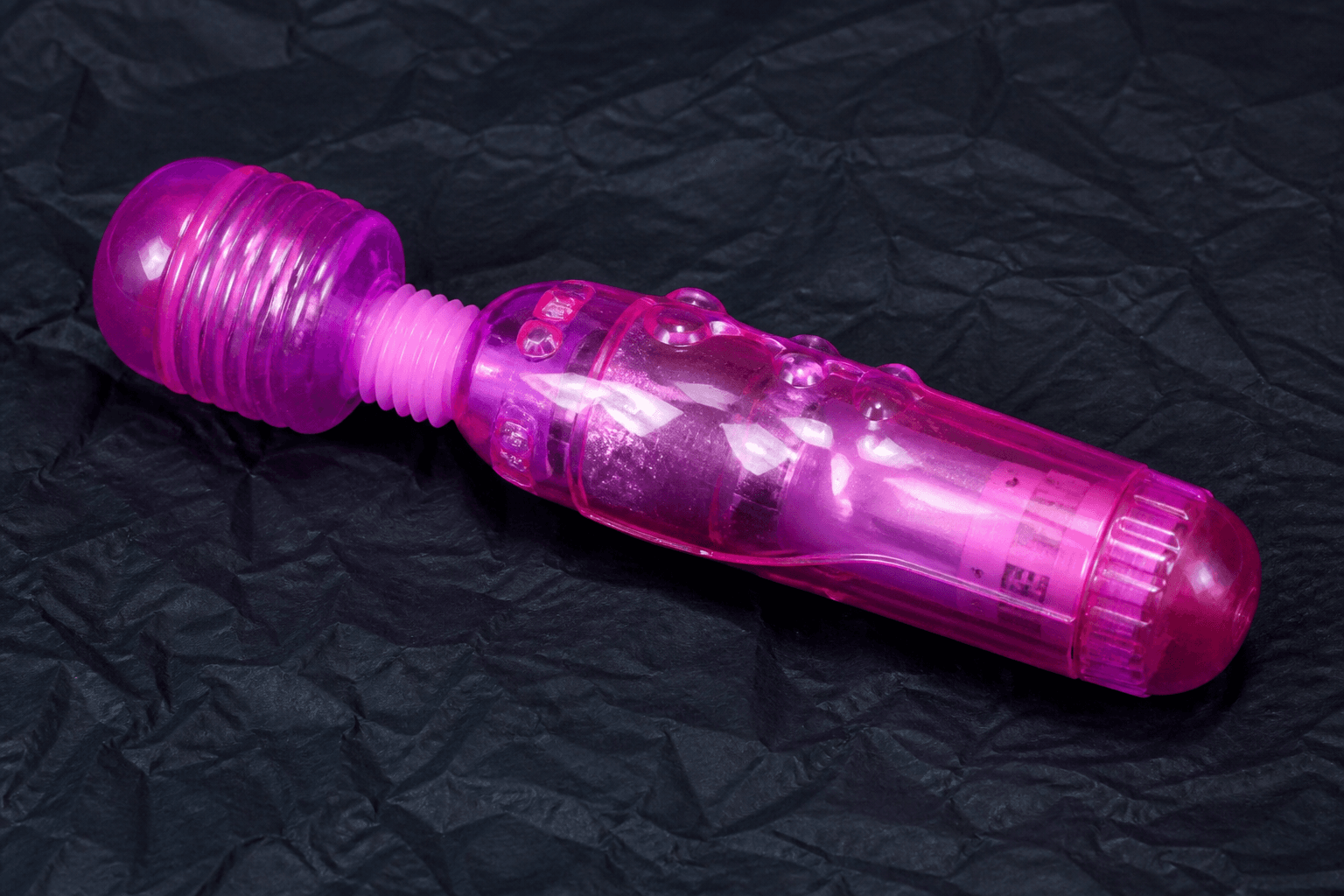 Editorial sample. Glossy translucent pink jelly wand on crumpled dark paper.