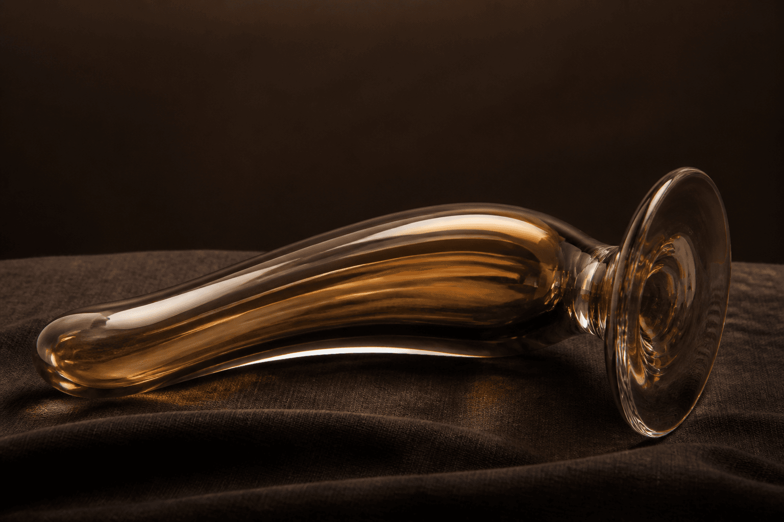 Studio shot of curved amber glass with a flared base on dark linen. Shape example, not a named SKU.