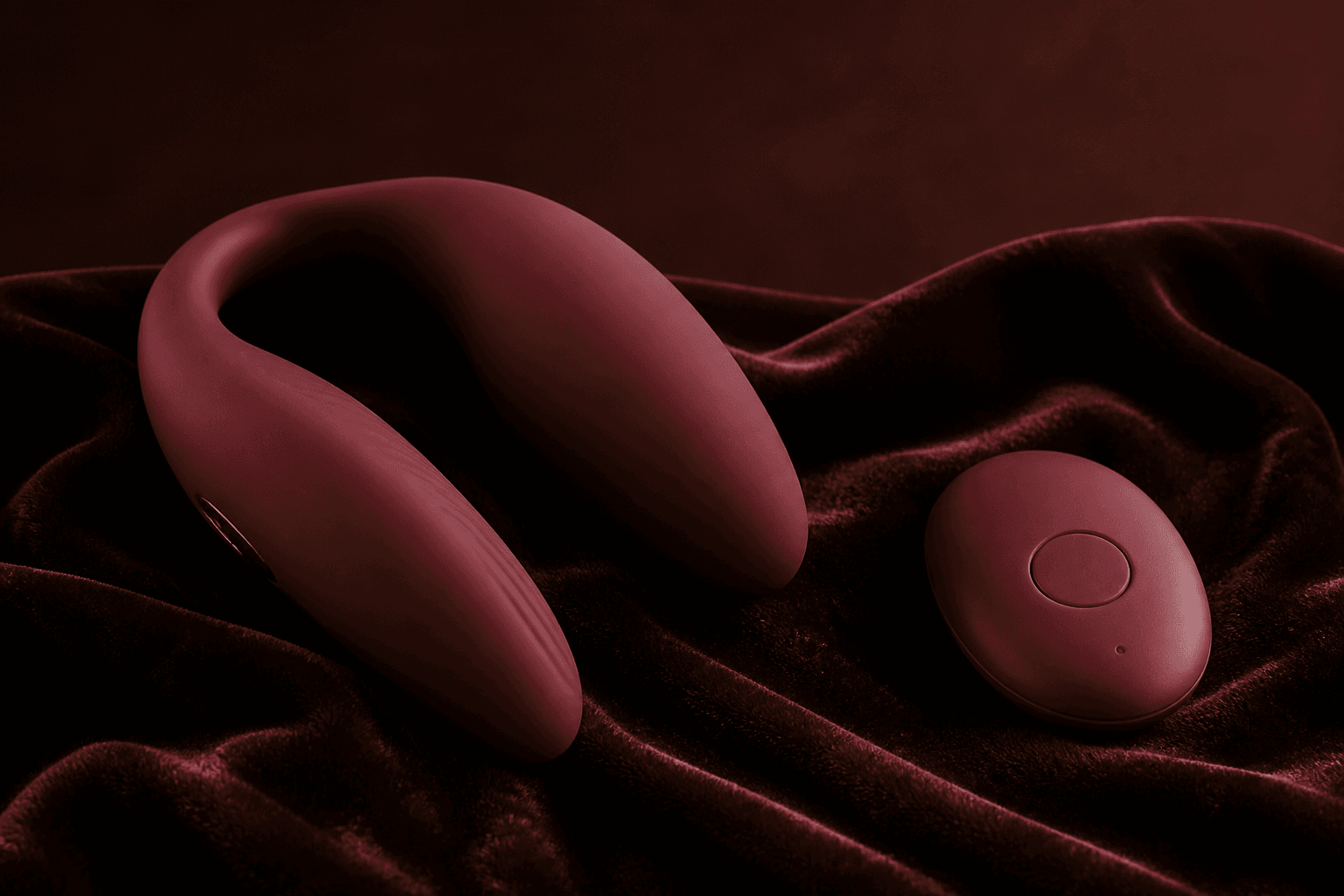 Editorial sample. Wine-colored wearable massager and a small remote on dark velvet.